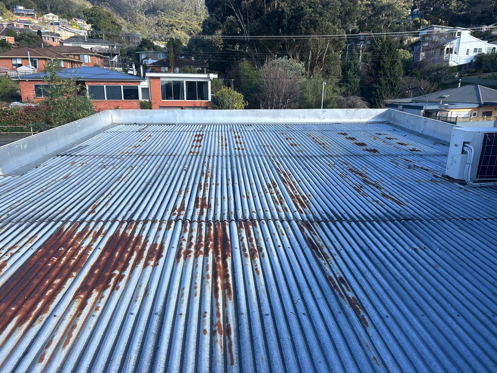 Existing corrugated metal roof with heavy rust staining, behind a parapet.