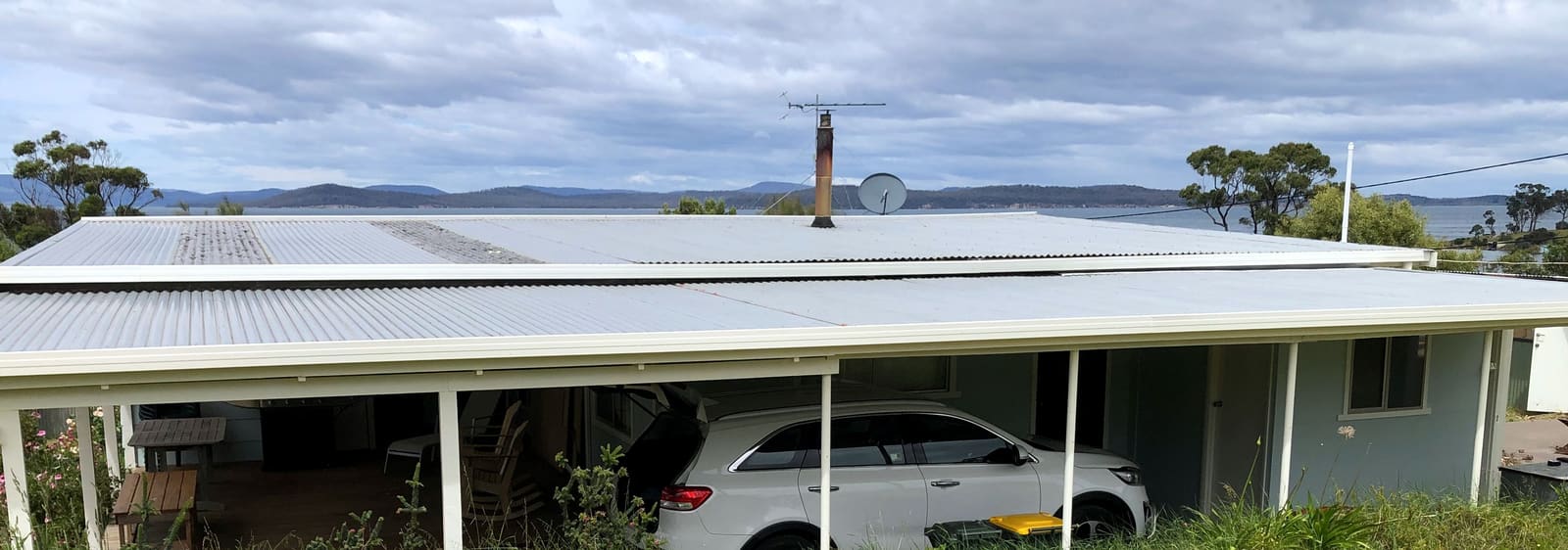 Single-storey house with a new light metal roof over the verandah and carport, water and hills behind.