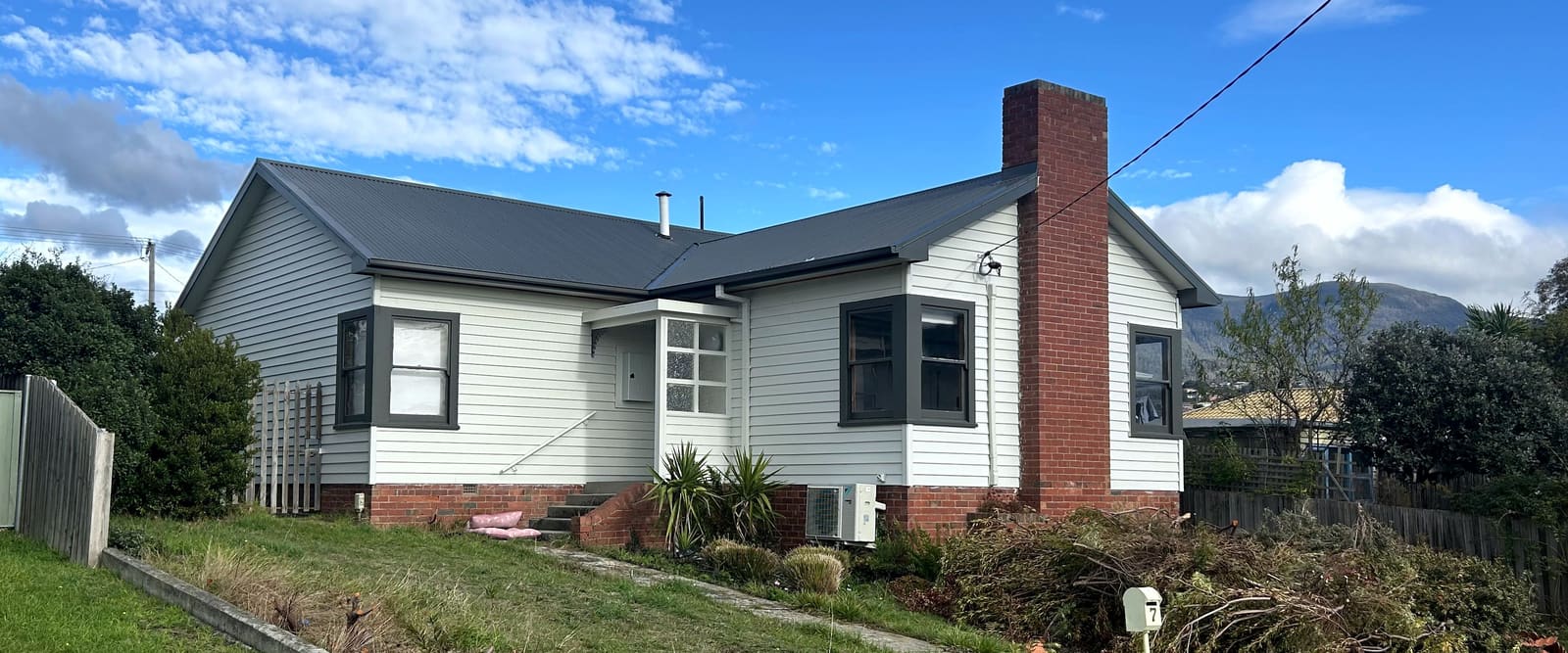 Weatherboard house with a newly installed dark corrugated metal roof and matching gutters, hills behind.